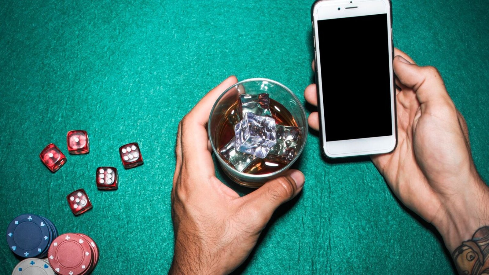 a man's hand holding cellphone and whisky glass over the poker table showing tthe top mobile casino games of 2024
